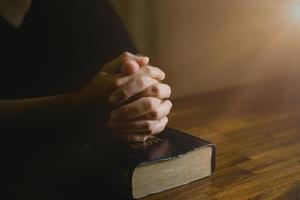 mano de persona de oración en fondo negro. la mujer católica cristiana está rezando a dios en la oscuridad en la iglesia. chica cree y fe en jesucristo. la religión de cristo y el cristianismo adoran o rezan concepto. foto