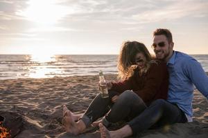 Young Couple Sitting On The Beach beside Campfire drinking beer photo