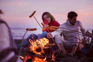 grupo de jóvenes amigos sentados junto al fuego en la playa foto