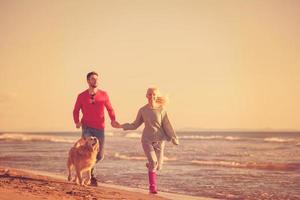 couple with dog having fun on beach on autmun day photo