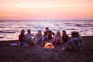 grupo de jóvenes amigos sentados junto al fuego en la playa foto