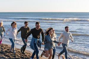 Group of friends running on beach during autumn day photo