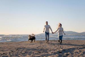 pareja con perro divirtiéndose en la playa el día del otoño foto