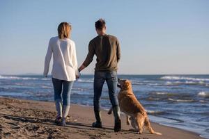 couple with dog having fun on beach on autmun day photo