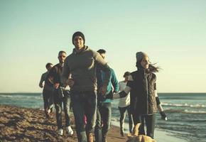 Group of friends running on beach during autumn day photo