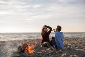 Young Couple Sitting On The Beach beside Campfire drinking beer photo