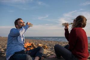 Young Couple Sitting On The Beach beside Campfire drinking beer photo