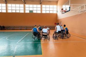 Disabled War veterans mixed race and age basketball teams in wheelchairs playing a training match in a sports gym hall. Handicapped people rehabilitation and inclusion concept photo