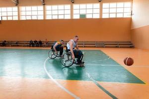 Disabled War veterans mixed race and age basketball teams in wheelchairs playing a training match in a sports gym hall. Handicapped people rehabilitation and inclusion concept photo