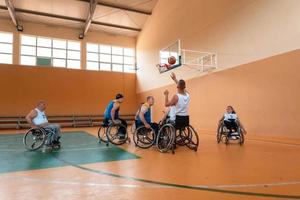 Disabled War veterans mixed race and age basketball teams in wheelchairs playing a training match in a sports gym hall. Handicapped people rehabilitation and inclusion concept photo