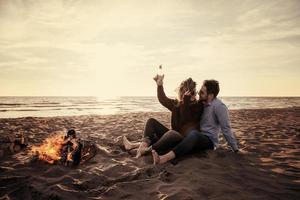 Young Couple Sitting On The Beach beside Campfire drinking beer photo