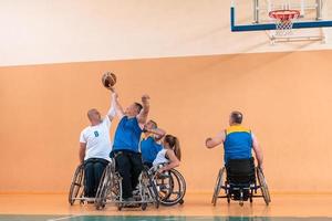 Disabled War veterans mixed race and age basketball teams in wheelchairs playing a training match in a sports gym hall. Handicapped people rehabilitation and inclusion concept photo