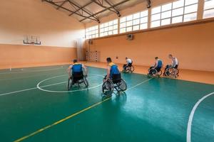 Disabled War veterans mixed race and age basketball teams in wheelchairs playing a training match in a sports gym hall. Handicapped people rehabilitation and inclusion concept photo