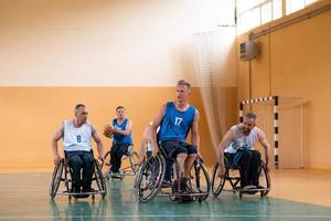 veteranos de guerra discapacitados de raza mixta que se oponen a equipos de baloncesto en sillas de ruedas fotografiados en acción mientras juegan un partido importante en una sala moderna. foto