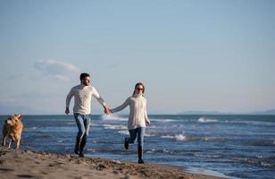 couple with dog having fun on beach on autmun day photo