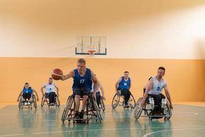 veteranos de guerra discapacitados de raza mixta que se oponen a equipos de baloncesto en sillas de ruedas fotografiados en acción mientras juegan un partido importante en una sala moderna. foto