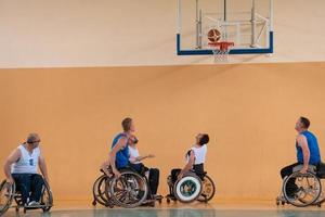 veteranos de guerra discapacitados de raza mixta que se oponen a equipos de baloncesto en sillas de ruedas fotografiados en acción mientras juegan un partido importante en una sala moderna. foto