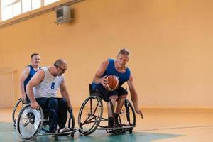 veteranos de guerra discapacitados de raza mixta que se oponen a equipos de baloncesto en sillas de ruedas fotografiados en acción mientras juegan un partido importante en una sala moderna. foto