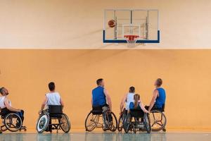 veteranos de guerra discapacitados de raza mixta que se oponen a equipos de baloncesto en sillas de ruedas fotografiados en acción mientras juegan un partido importante en una sala moderna. foto