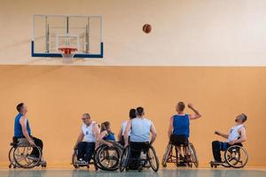 veteranos de guerra discapacitados de raza mixta que se oponen a equipos de baloncesto en sillas de ruedas fotografiados en acción mientras juegan un partido importante en una sala moderna. foto