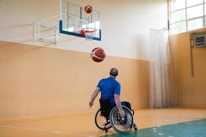 un inválido de guerra en silla de ruedas entrena con una pelota en un club de baloncesto en entrenamiento con equipo deportivo profesional para discapacitados. el concepto de deporte para personas con discapacidad foto