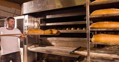 trabajador de panadería sacando panes recién horneados foto