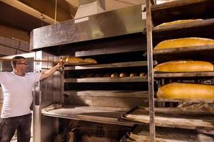 trabajador de panadería sacando panes recién horneados foto