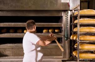 trabajador de panadería sacando panes recién horneados foto