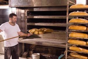 trabajador de panadería sacando panes recién horneados foto