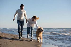 couple with dog having fun on beach on autmun day photo