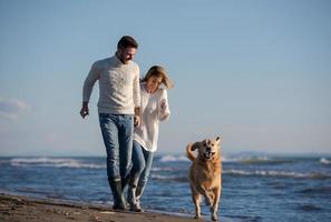 pareja con perro divirtiéndose en la playa el día del otoño foto