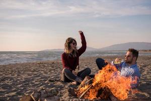 Young Couple Sitting On The Beach beside Campfire drinking beer photo