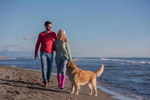 pareja con perro divirtiéndose en la playa el día del otoño foto