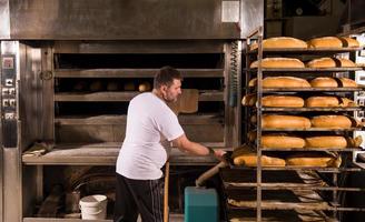 trabajador de panadería sacando panes recién horneados foto