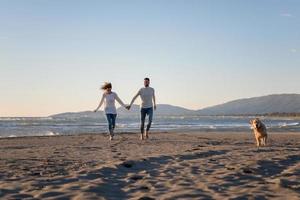 couple with dog having fun on beach on autmun day photo