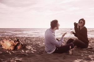 Young Couple Sitting On The Beach beside Campfire drinking beer photo