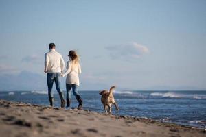 couple with dog having fun on beach on autmun day photo