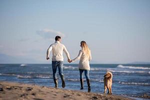 couple with dog having fun on beach on autmun day photo