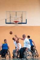 Disabled War veterans mixed race and age basketball teams in wheelchairs playing a training match in a sports gym hall. Handicapped people rehabilitation and inclusion concept photo