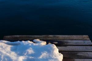 wooden pier with snow on dark water background photo