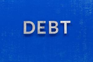 the word debt layed on blue painted board with thick silver metal aphabet characters photo