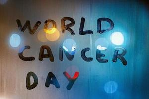 las palabras día mundial del cáncer escritas a mano en vidrio húmedo nocturno - primer plano con desenfoque de fondo foto