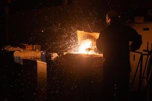 steelworker removing slag from steel furnace with sparks and smoke exhaust photo