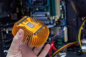 caucasian hand holding orange plated computer heatsink and pc internals in blurry background photo