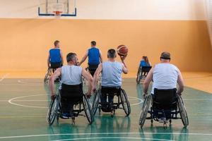 veteranos de guerra discapacitados de raza mixta que se oponen a equipos de baloncesto en sillas de ruedas fotografiados en acción mientras juegan un partido importante en una sala moderna. foto