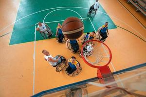 veteranos de guerra o de trabajo discapacitados equipos mixtos de baloncesto de raza y edad en sillas de ruedas jugando un partido de entrenamiento en un gimnasio deportivo. concepto de rehabilitación e inclusión de personas con discapacidad. foto