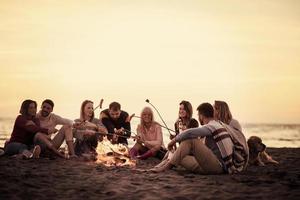 grupo de jóvenes amigos sentados junto al fuego en la playa foto