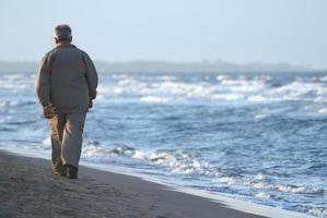 lonely older  man walking on beach photo