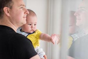 young father holding baby near the window at home photo