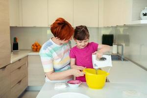 Funny little girl helper playing with dough on his hands learning to knead helps adult mom in the kitchen, happy cute baby daughter and parent mom have fun cooking cookies. photo